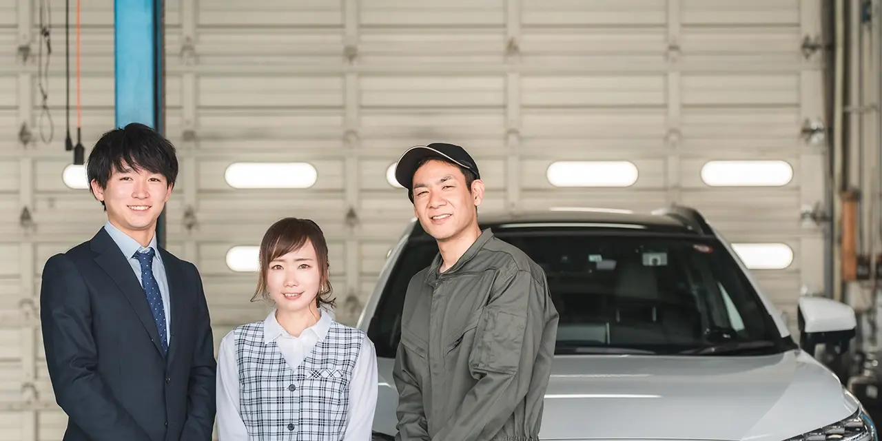 笑顔で並ぶスーツ姿の男性、事務室の女性、作業服の整備士